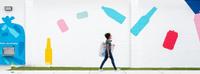 Woman Walking in Front of a Bottle and Can Mural